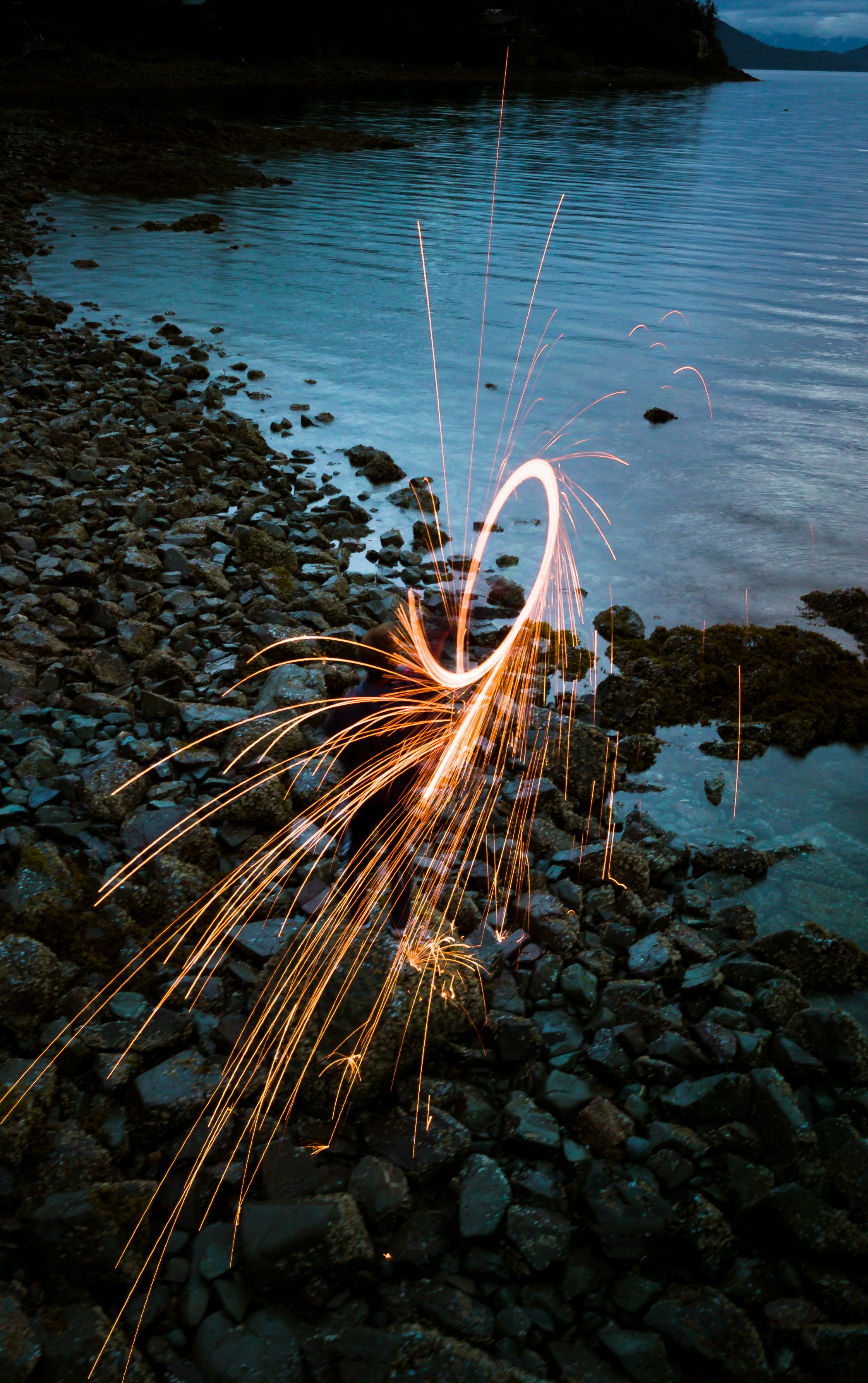 person standing on rock formation near body of water on steel wool photography